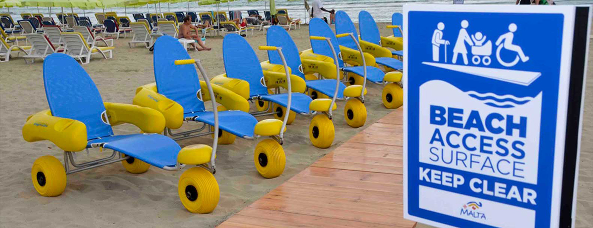 [photo: beach with boardwalk and a row of wheeled loungers, sign reads: Beach Access Surface. Keep Clear”]