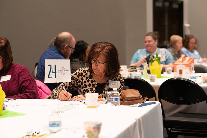 Candid photo of a breakfast event attendee at her table, completing a pledge card.