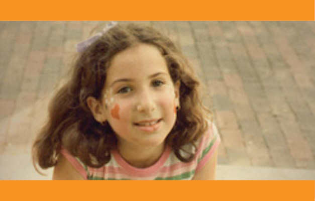 Young, light-skinned, brunette girl sitting outside and smiling. 